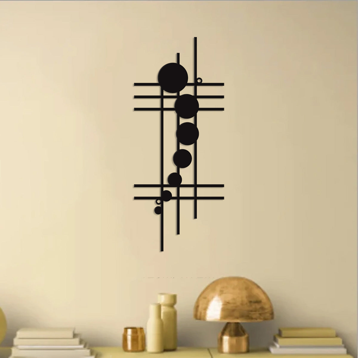 Decorative wall art with geometric design on a beige wall above a shelf with books and a lamp.